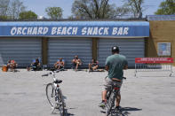 People take in the sun and relax in front of a closed snack bar at Orchard Beach in the Bronx borough of New York, Sunday, May 17, 2020. Parks, boardwalks and beaches attracted some crowds this weekend, though city beaches aren't officially open and won't be for the upcoming Memorial Day weekend. New York City Mayor Bill de Blasio said the city's beaches could be closed off completely to public access if people don't follow social distancing rules. Fencing is being installed at entrance ways and could be rolled out if beaches — meant now only for nearby residents to get some exercise — get overcrowded or people violate swimming bans, he said. (AP Photo/Seth Wenig)