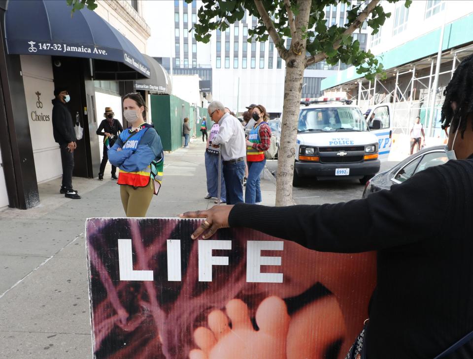 A group of volunteer clinic escorts (in multi colored vests), stand outside of Choices Women's Medical Center off of Jamaica Avenue in Queens, as abortion protesters hold signs June 18, 2022. The escorts walk with patients to the clinic, when they are sometimes confronted by abortion protesters gathered at the site. 