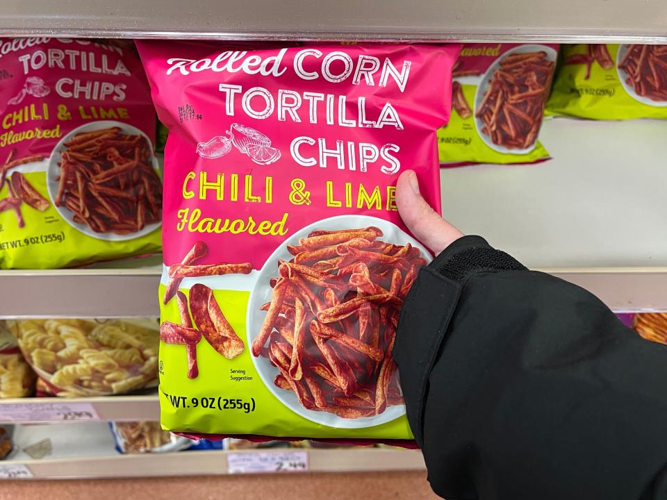 The writer holds a bright-pink and green bag of Trader Joe's rolled-corn chili-lime tortilla chips