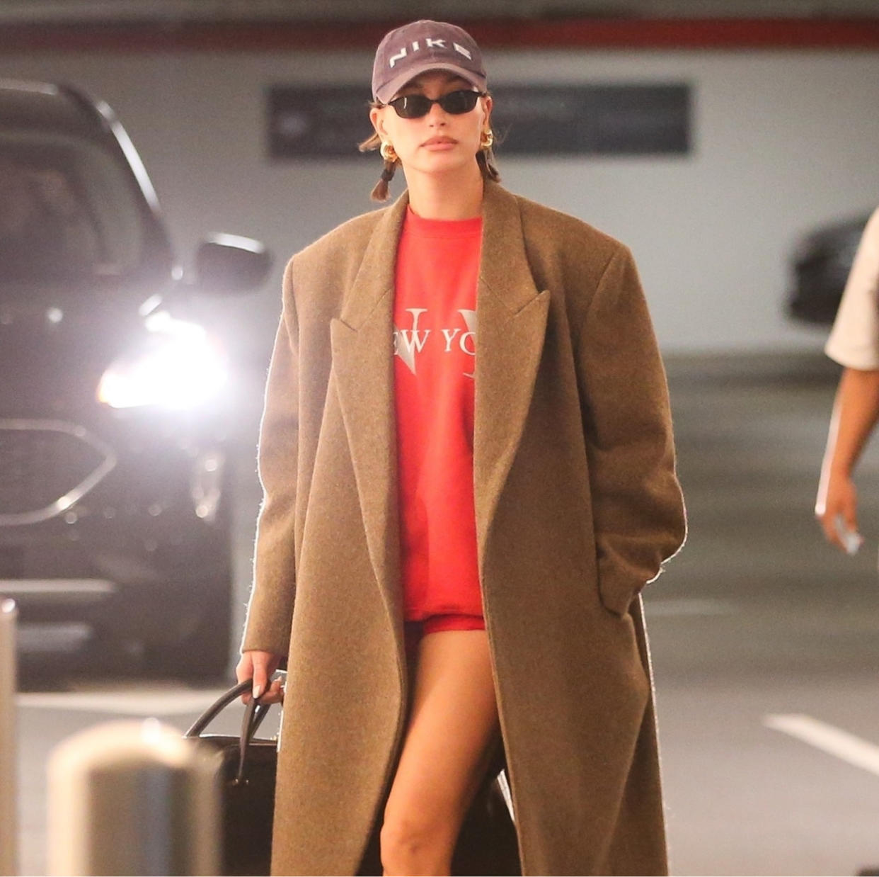  Hailey Bieber in red micro shorts, a red sweatshirt, and tan maxi coat. 