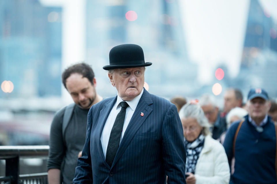 Focus on an older man in a hat, suit, and tie waiting in line