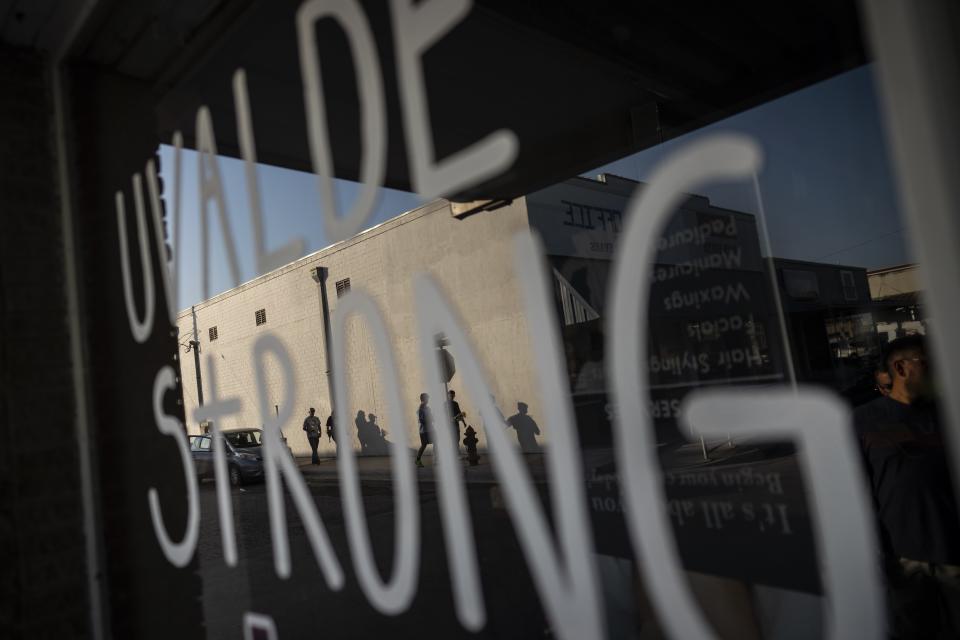 People are seen through a reflection off the window of a beauty school where a sign that reads "Uvalde Strong" is painted, days after a deadly school shooting took the lives of 19 children and two teachers, on Sunday, May 29, 2022, in Uvalde, Texas. (AP Photo/Wong Maye-E)