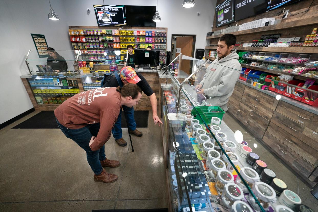 Cody Mathis, 31, of Crystal Lake, Ohio, left, looks at the cannabis products with his friend Robert Moore, 65, of Vandalia, Ohio, at House of Dank on Fort Street in Detroit on Jan. 4, 2023, as budtender Raven Campbell, 32, looks on from the right. After years of delay, recreational marijuana finally went on sale in Detroit.