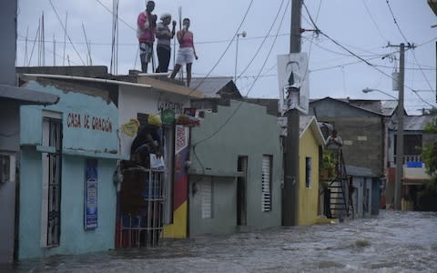 People look down on a flooded street from a roof in Santiago de los Caballeros, Dominican Republic - Credit: Luis Tavarez