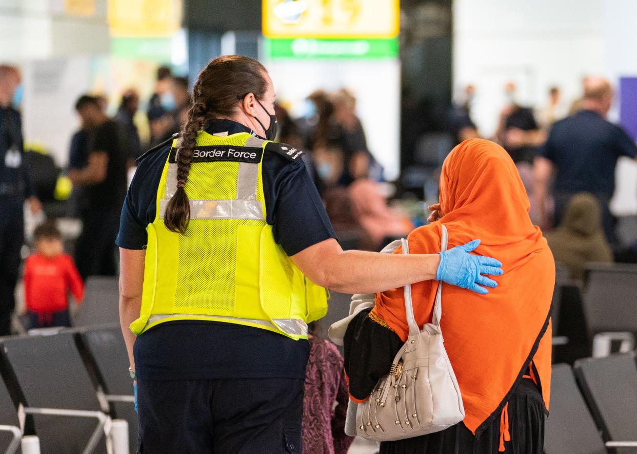 A member of Border Force staff (L) assists an Afghan refugee on her arrival on an evacuation flight from Afghanistan, at Heathrow Airport, London on August 26, 2021. - A terrorist threat against Kabul airport is 