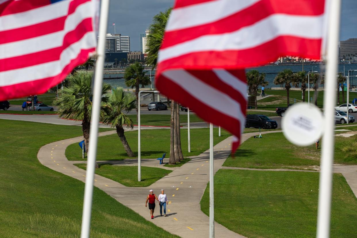 People walk on a sidewalk below the Flags for Heroes display at Cole Park on Veterans Day in Corpus Christi, Texas, on Friday, Nov. 11, 2022.