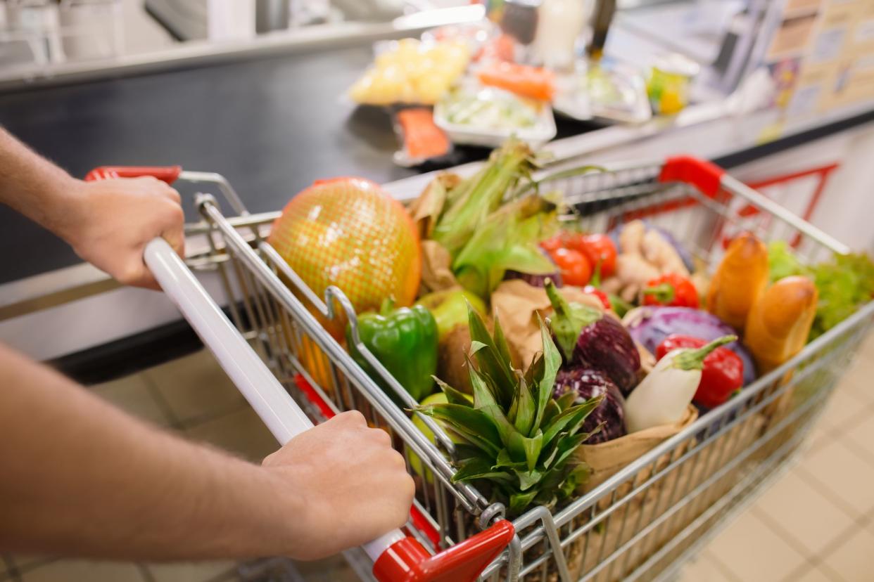 A customer with a shopping cart while checking out at a food store.