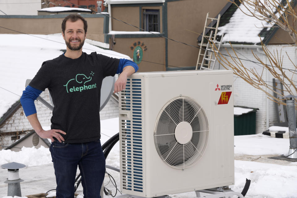 David Richardson, the co-founder of Elephant Energy, leans on a condenser placed on the roof during the installation of a heat pump in an 80-year-old rowhouse in a neighborhood Friday, Jan. 20, 2023, in northwest Denver. (AP Photo/David Zalubowski)