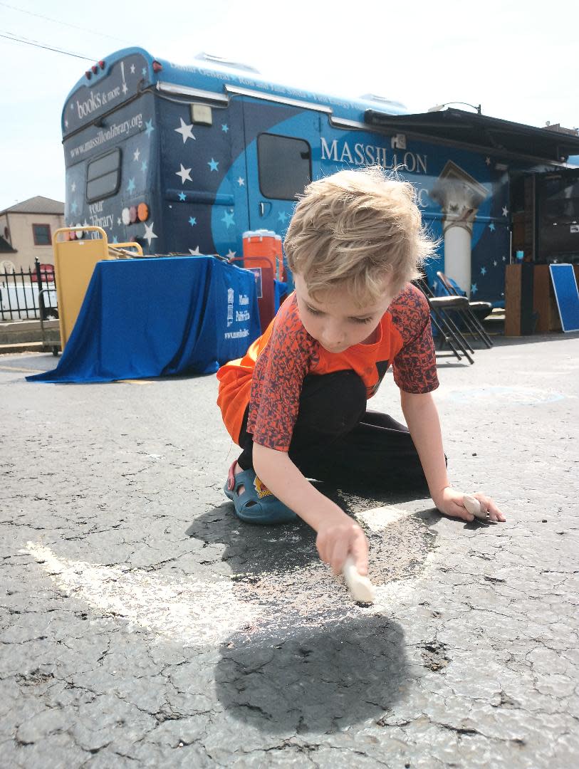 Whit Ridgley, 6, of Massillon, draws a half-moon Monday afternoon on the parking lot pavement of the Massillon Public Library. The library hosted an eclipse watch party that included free beverages and safety glasses.