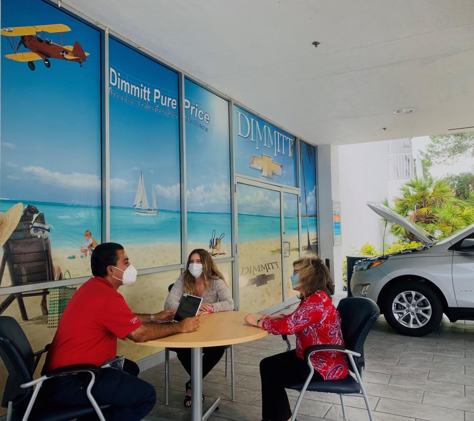 Dimmitt Chevrolet sales associate Raheel Syeld reviews the features on a new Chevrolet Equinox SUV with two customers in an outdoor office area during the coronavirus pandemic.