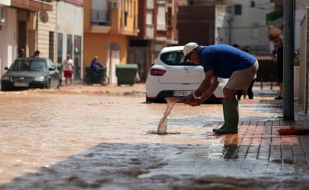 A man cleans a garden accessory on a partially flooded street after heavy rains in San Pedro del Pinatar