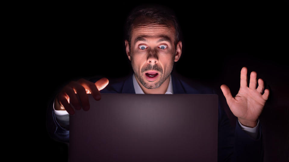 Businessman staring at laptop with frightened face in the dark