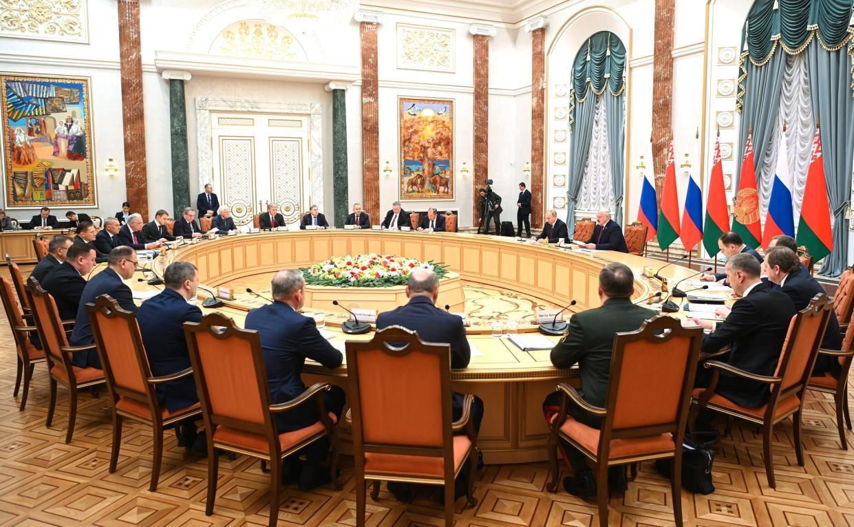 Putin and Lukashenko sit with about two dozen others at a meeting.