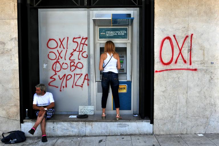 A woman withdraws money from an ATM machine next to a beggar and graffiti reading "No to fear", in Thessaloniki on July 6, 2015