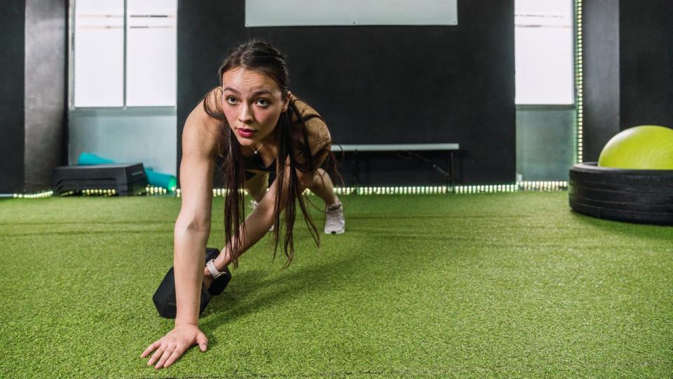 Woman performs plank drag with dumbbell