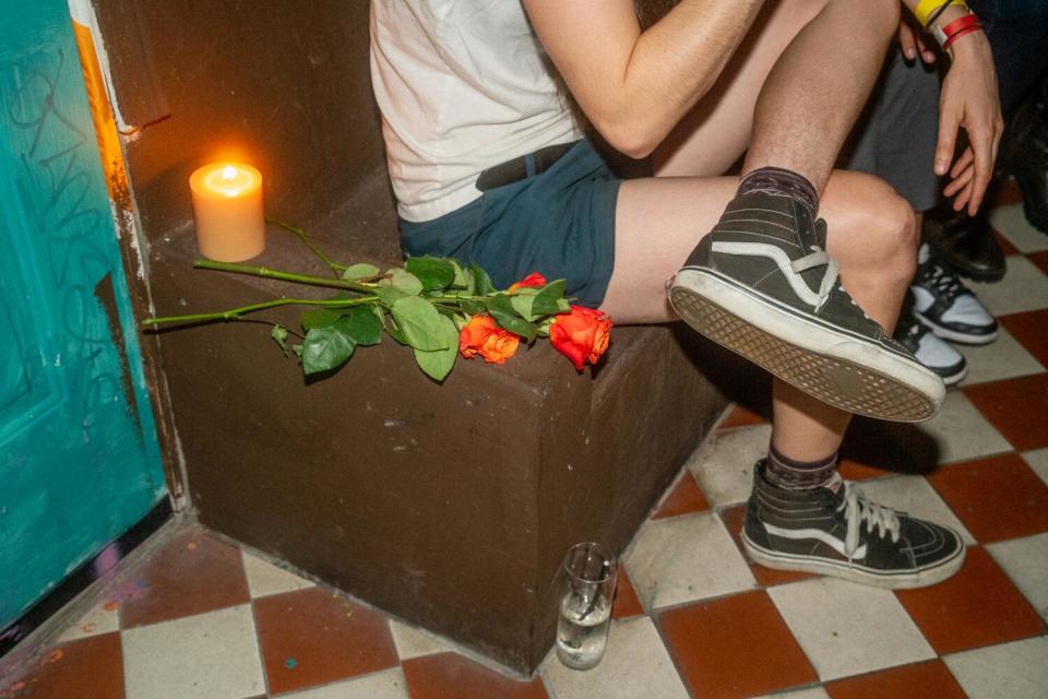 Roses and a burning candle on a bench next to a person who is visible from the shoulders down.