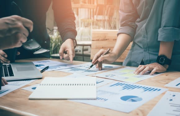 Multiple people performing market research with papers spread across a table