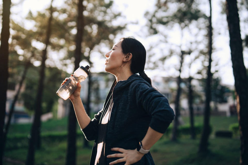 Young Asian sports woman taking a rest and drinking water from reusable water bottle after jogging outdoors in park. Taking water break. Staying hydrated. Fitness goal. Wellbeing and wellness. Health and fitness training routine. Healthy living lifestyle