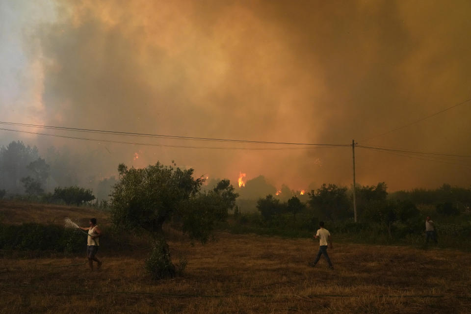 Men use a garden hose to try to deter a fast approaching forest fire before quickly giving up in the village of Bemposta, near Ansiao, central Portugal, Wednesday, July 13, 2022. Thousands of firefighters in Portugal continue to battle fires all over the country that forced the evacuation of dozens of people from their homes. (AP Photo/Armando Franca)