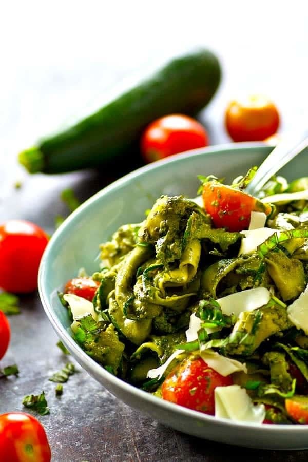 Tomatoes, shaved zucchini, and cheese covered in pesto in a blue bowl