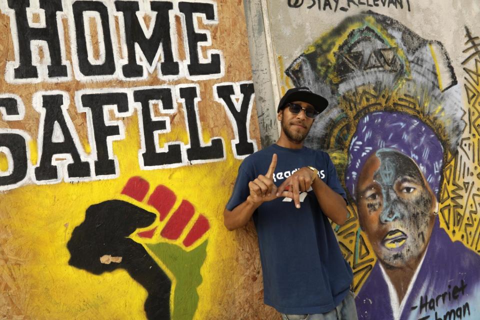 A man makes an L.A. sign with his hands in front of a mural