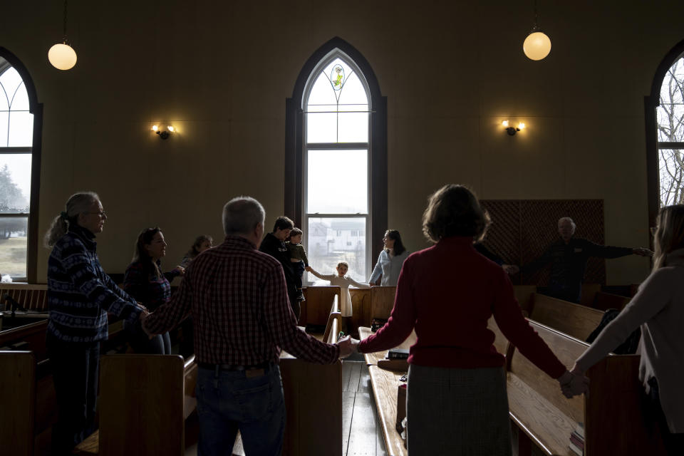 Congregants join hands at the conclusion of a service at Elmore United Methodist Church, Sunday, March 3, 2024, in Elmore, Vt. In pockets of New England, democracy is done a bit differently. People can still participate directly and in person. One day each year, townsfolk gather at their annual Town Meeting to hash out local issues. They talk, listen, debate, vote. And in places like Elmore, once it's all over, they sit down together for a potluck lunch.. (AP Photo/David Goldman)