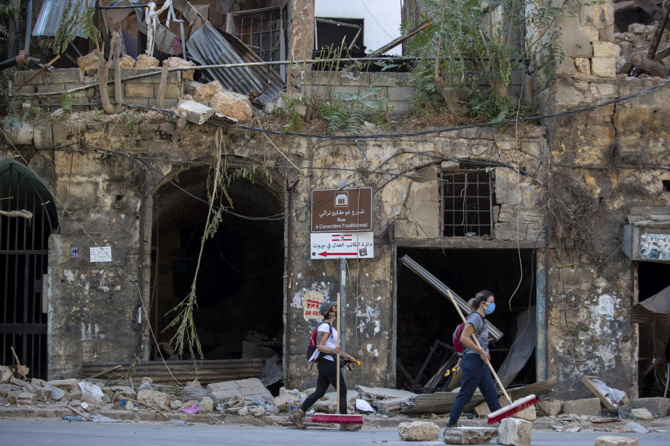 Mujeres con escobas pasan caminando frente a un inmueble histórico dañado por la explosión del martes en el barrio de Gemmayzeh, en Beirut, el sábado 8 de agosto de 2020. (AP Foto/Hassan Ammar)