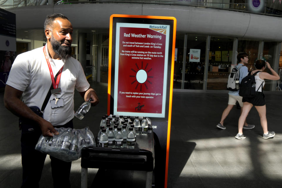 FILE - A railway worker hands out bottles of water to passengers at King's Cross railway station where there are train cancellations due to the heat in London, July 19, 2022. What's considered officially “dangerous heat” in coming decades will likely hit much of the world at least three times more often as climate change worsens, according to a new study. (AP Photo/Kirsty Wigglesworth, File)