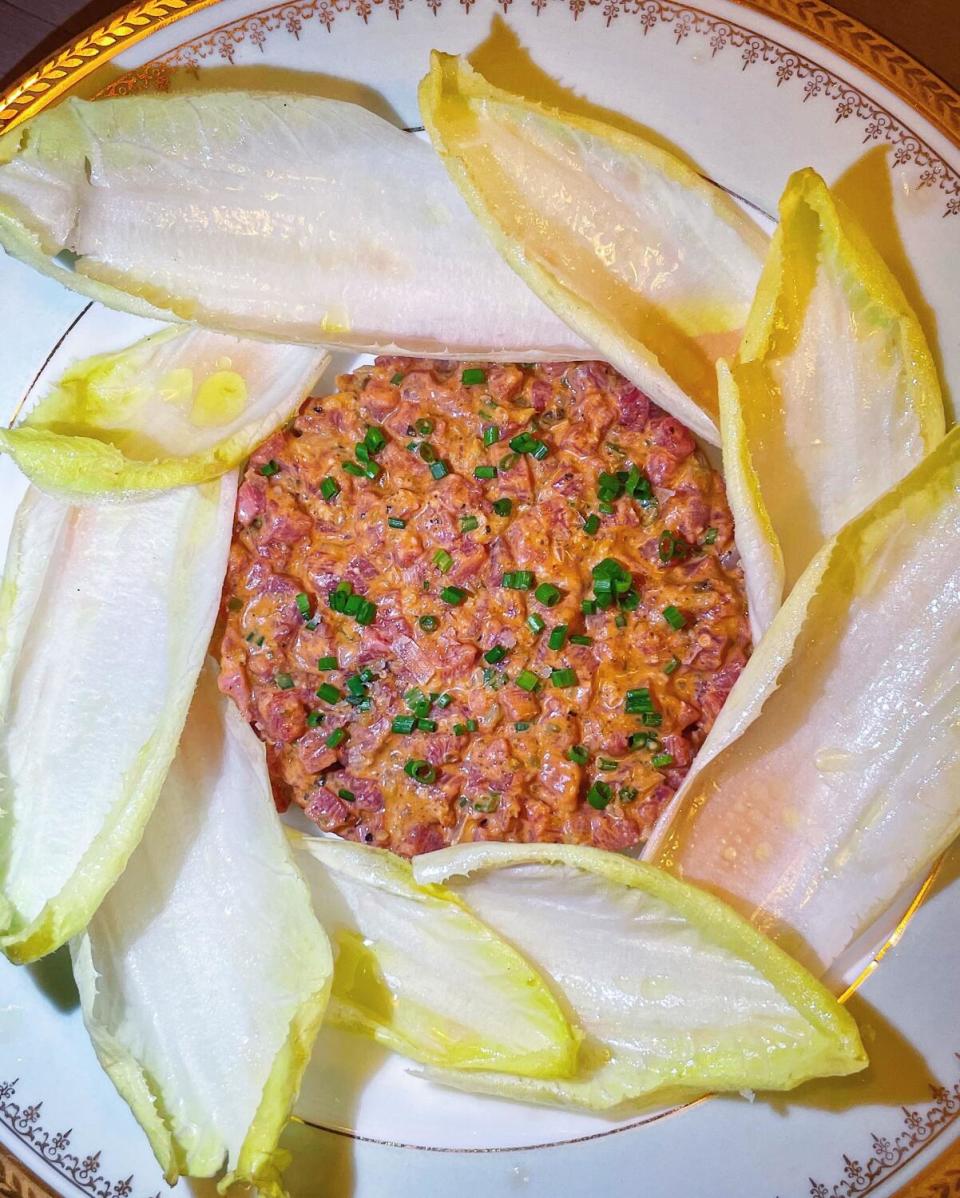 An overhead photo of a circle of chive-topped steak tartare surrounded by endive leaves