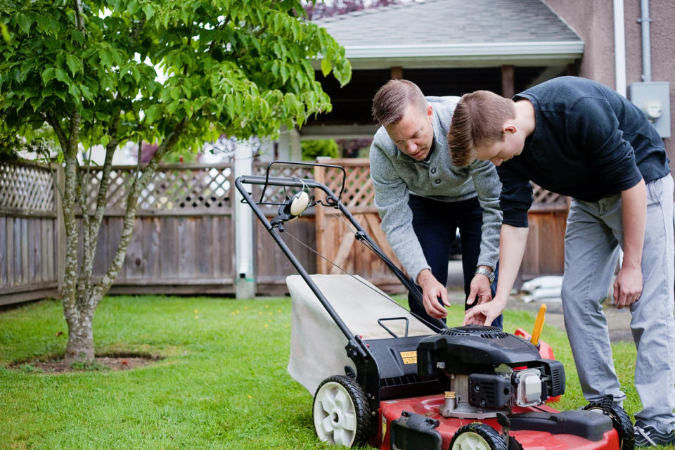 A man and a teenage boy are inspecting a lawn mower in a back yard.