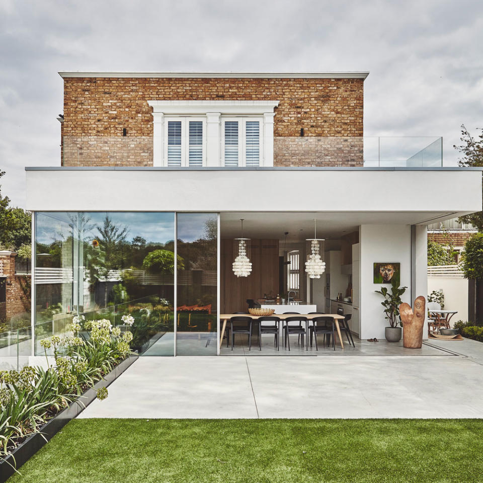 open plan brick house with outside flower décor and a grass lawn glass sliding doors with hanging glass chandeliers