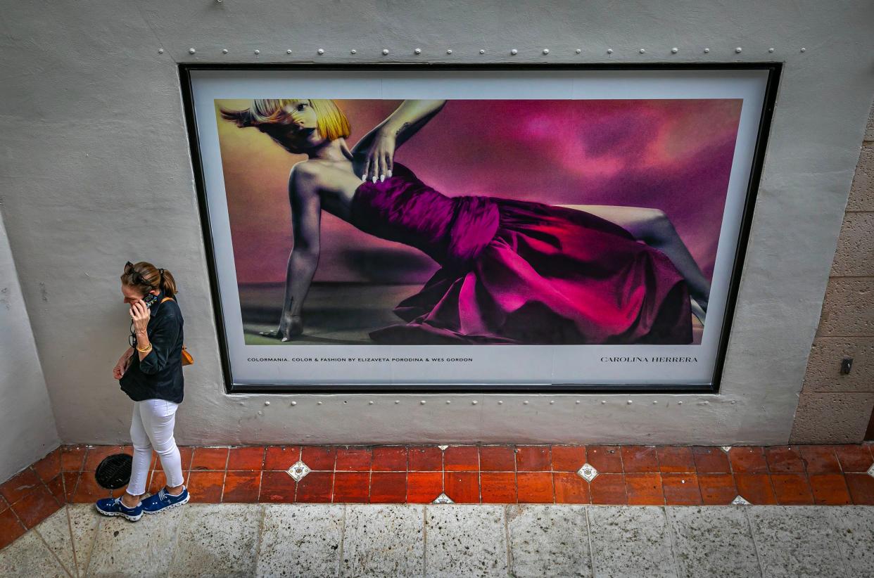 A woman talks on her cell phone in the Esplanade Shopping Mall next to a Carolina Herrera ad Friday, February 23, 2024.