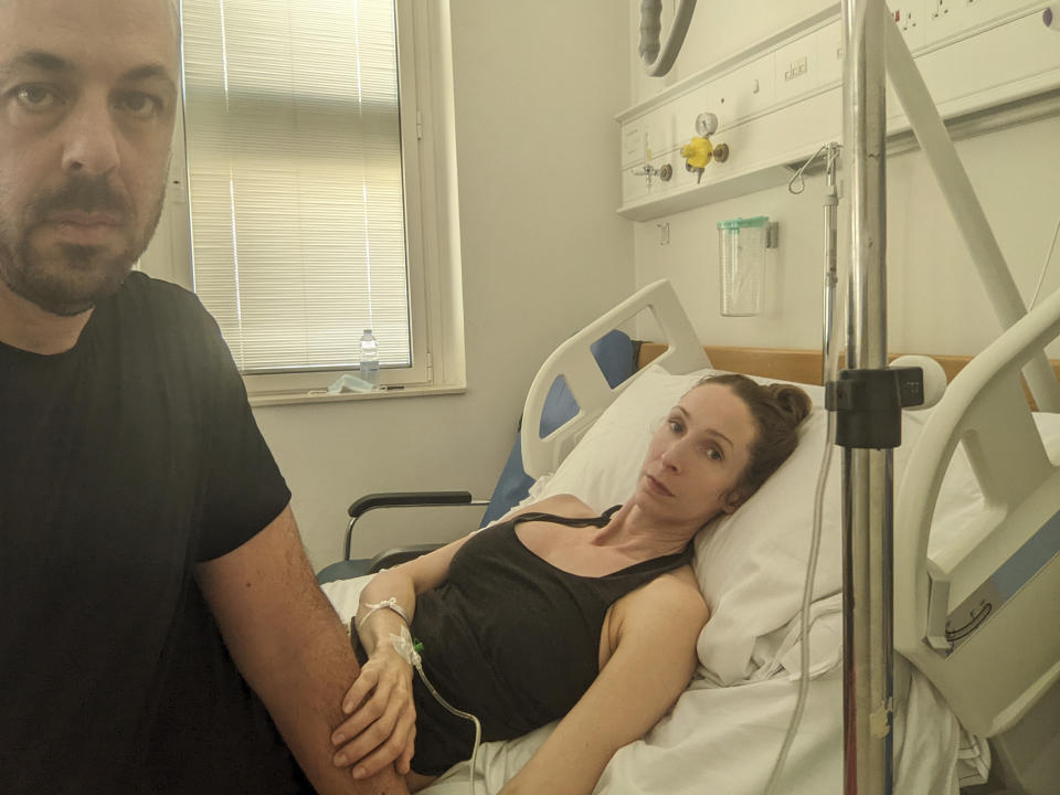 Andrea Prudente, 38, who suffered an incomplete miscarriage while vacationing in Malta lies in her bed at the Mater Dei Hospital in Msida, Malta, comforted by her partner Jay Weeldreyer, left, Thursday, June 23, 2022. Prudente will be airlifted to a Spanish island on Thursday for a procedure to prevent infection because Maltese law prohibits abortion under any circumstances, the woman's partner said. (Jay Weeldreyer via AP)