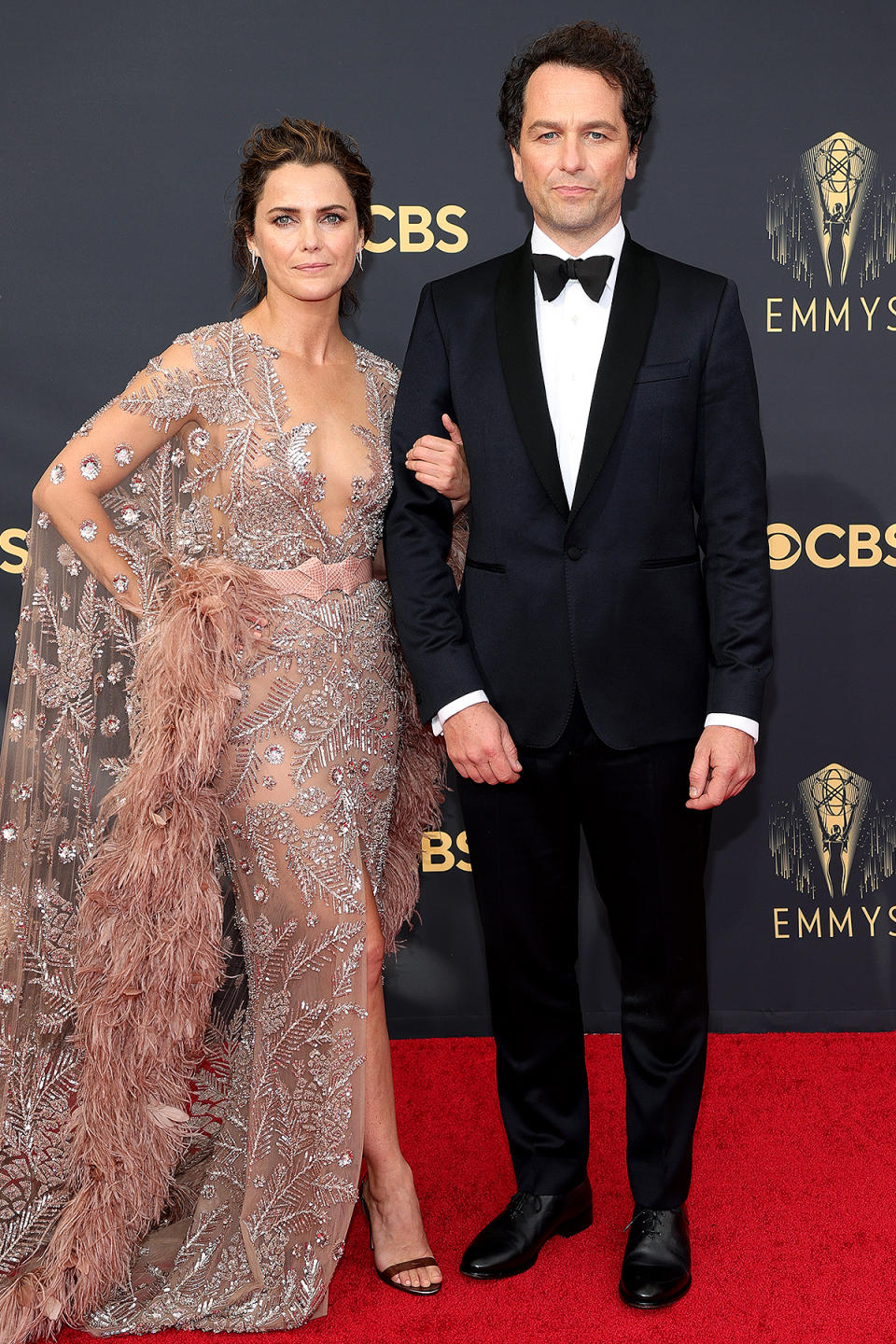 <p>The couple, who starred in <em>The Americans </em>together from 2014 to 2018, channeled Old Hollywood glamour with their red carpet looks. Rhys wore a classic black tux, which Russell pulled out all the stops in a sheer, sequined gown including feather sleeves. </p>