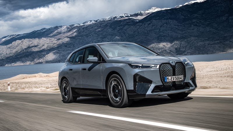 Front view of the BMW iX in motion on a road near a lake.