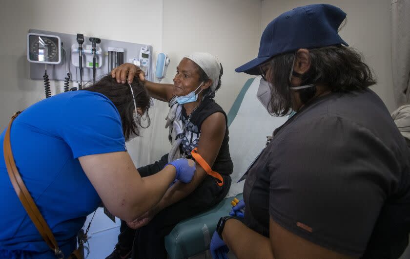 PACOIMA, CA - September 26, 2022 - Patient Yesenia Guevara, center, adjusts LVN Munisa Saidova's face mask, left, as Saidova draws blood with RN Richelle Legaspi,(CQ) right, inside a mobile medical clinic set up by the L.A. County Department of Health Services in a parking lot at Richie Valens Park Sept. 26, 2022 in Pacoima, CA. (Brian van der Brug / Los Angeles Times)