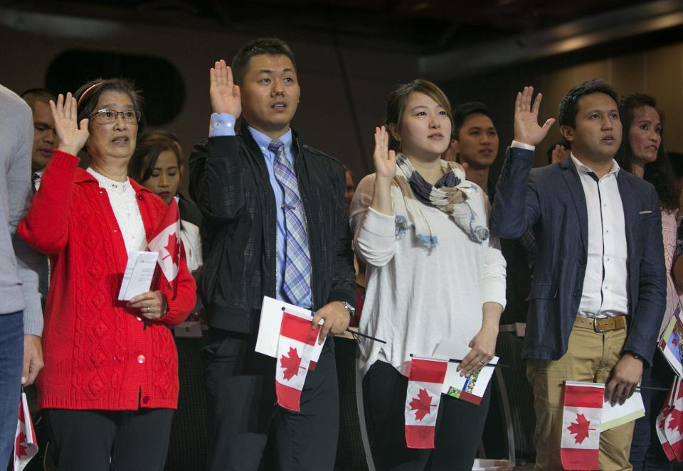 People at a Canadian citizenship ceremony swear their allegiance to Canada while holding Canadian flags