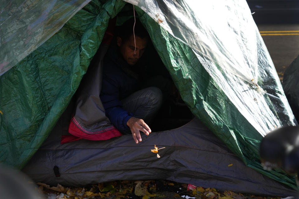 A migrant man removes a small leaf from his tent in a small tent community, Wednesday, Nov. 1, 2023, near a Northside police station in Chicago. (AP Photo/Charles Rex Arbogast)