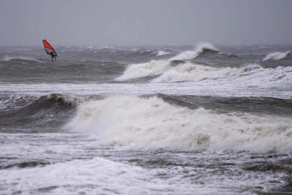 A wind surfer rides on waves at the Baltic Sea near Kuehlungsborn, Germany, Friday, Oct. 20, 2023. Gale-force winds and floods struck several countries in Northern Europe as the region endured more heavy rain on Friday that forecasters say will continue into the weekend. (AP Photo/Matthias Schrader)