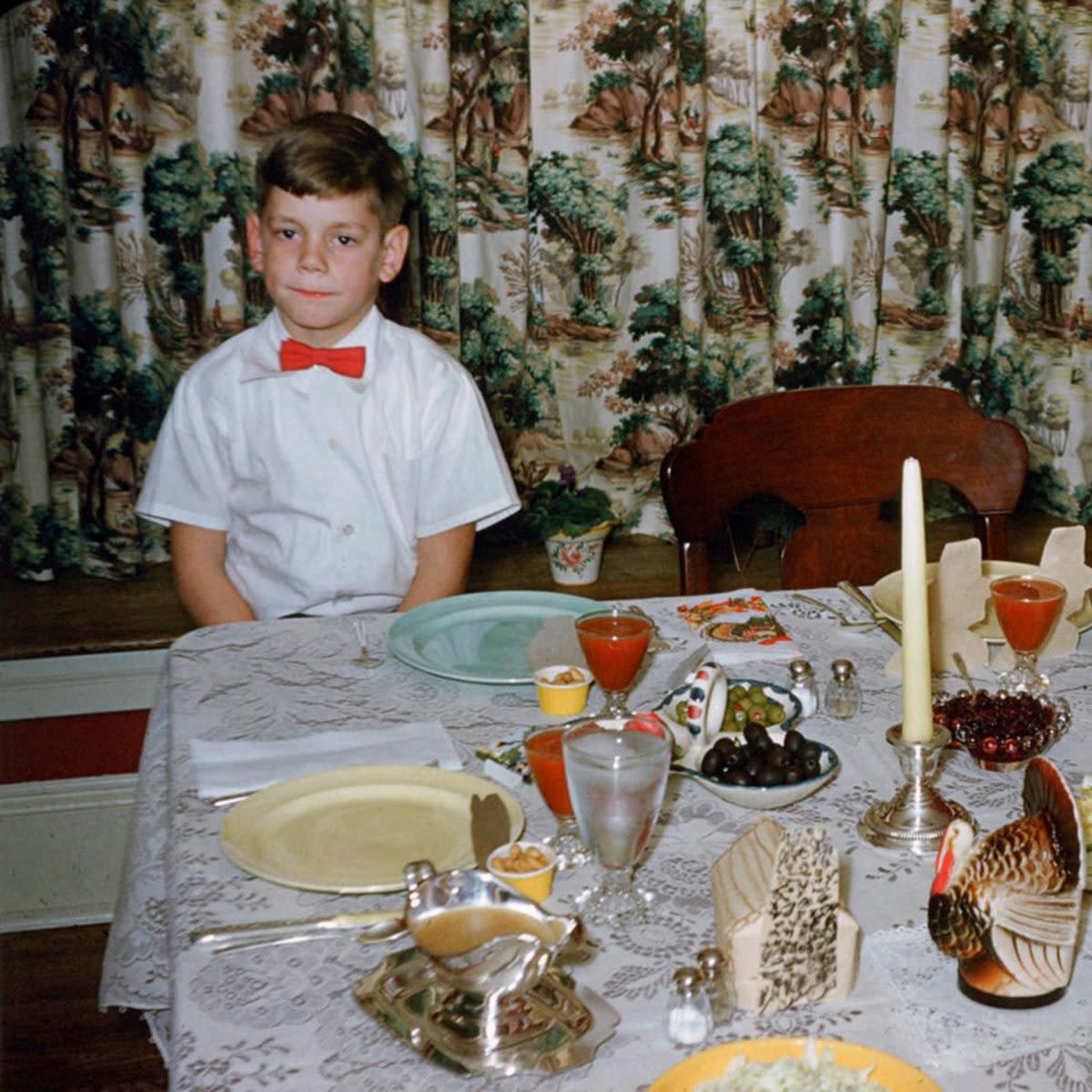 bored boy in red bow tie sits patenintly at thanksgiving dinner table