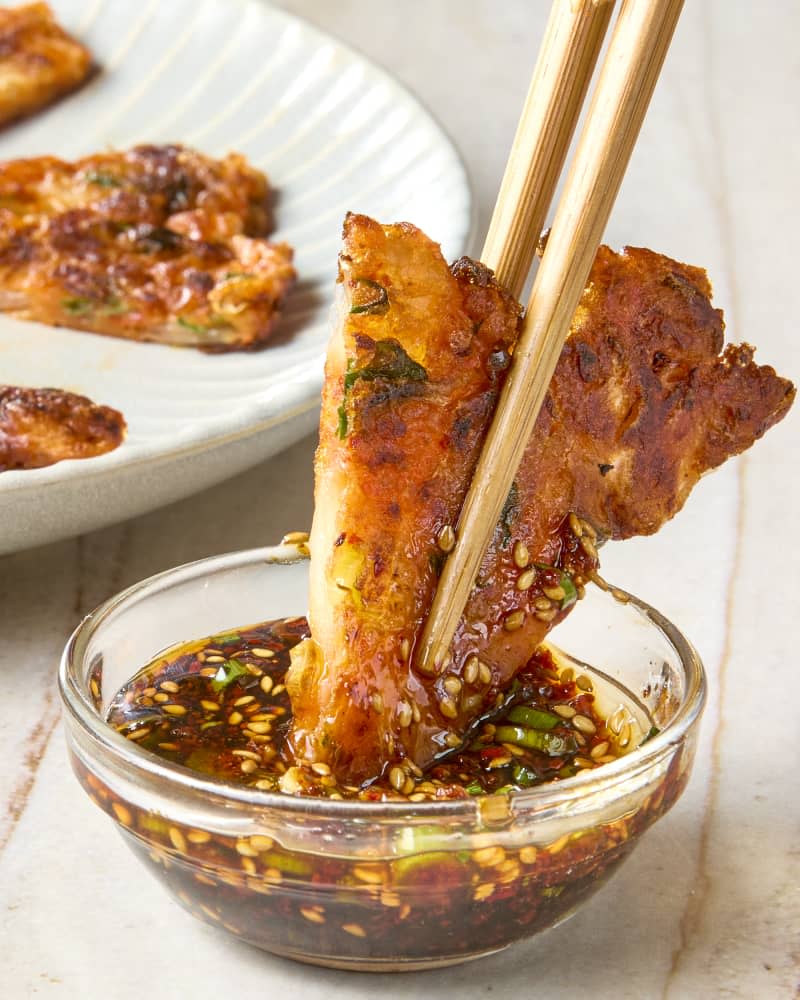 head on shot of a kimchi pancake being dipped into the dipping sauce using chopsticks