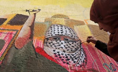 A Palestinian woman paints a mural, depicting a masked Palestinian holding a knife, in support of Palestinians committing stabbing attacks against Israelis, in Rafah in the southern Gaza Strip November 3, 2015. REUTERS/Ibraheem Abu Mustafa