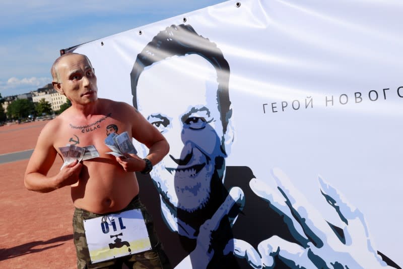 A protester wearing a mask of Russian President Vladimir Putin holds fake bank notes as he stands in front of a poster of Alexei Navalny ahead of a meeting between U.S. President Joe Biden and Russian President Vladimir Putin in Geneva
