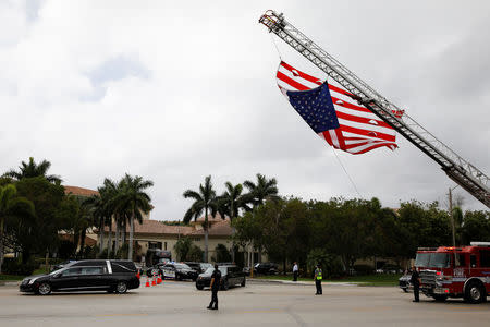 A hearse carrying the casket of Aaron Feis, one of the victims of the mass shooting at Marjory Stoneman Douglas High School, drives past a U.S. flag, placed on a fire truck, during his funeral service in Coral Springs, Florida, U.S., February 22, 2018. REUTERS/Carlos Garcia Rawlins