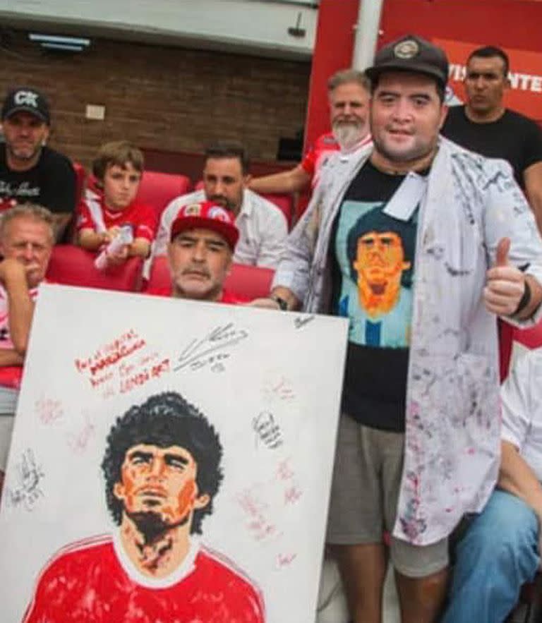Cristian Landi, con Diego Maradona, mostrando la pintura que hizo del 10