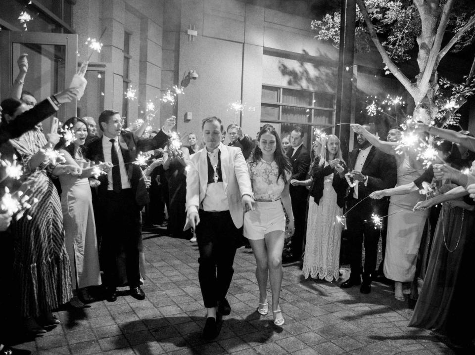 A bride and groom leave their wedding as their guests raise sparklers around them.