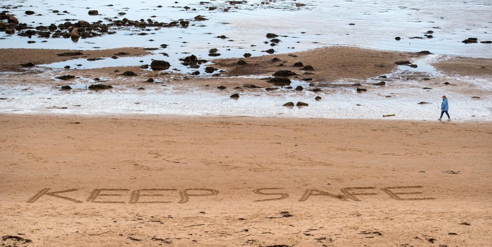 A person walks past the words "Stay Safe", etched into the sand on the beach in Whitley Bay, north east England on April 30, 2020, as life in Britain continues during the nationwide lockdown to combat the novel coronavirus pandemic. - Britain is "past the peak" of its coronavirus outbreak, Prime Minister Boris Johnson said Thursday, despite recording another 674 deaths in the last 24 hours, taking the toll to 26,711. "For the first time, we are past the peak of this disease... and we are on the downward slope," Johnson said in his first media briefing since returning to work following his own fight against the virus. (Photo by Oli SCARFF / AFP) (Photo by OLI SCARFF/AFP via Getty Images)