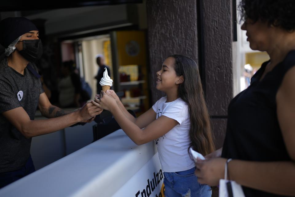 A vendor hands Valerie Torres an ice cream cone accompanied by her mother Francys Brito, in Caracas, Venezuela, Sunday, Feb. 26, 2023. “Sometimes she asks, ‘Why do people not like Maduro?’” said Brito. “Well because, thank God, you have everything, but there are many people who don’t," she tells Valerie. (AP Photo/Ariana Cubillos)