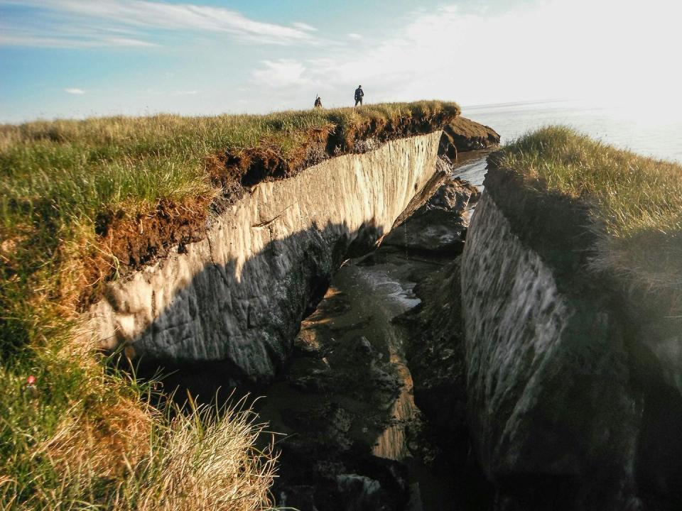 Two people stand on a cliff where the permafrost is visible.