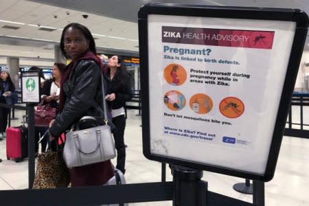 A woman looks at a Center for Disease Control (CDC) health advisory sign about the dangers of the Zika virus as she lines up for a security screening at Miami International Airport in Miami, Florida, U.S., May 23, 2016.  REUTERS/Carlo Allegri